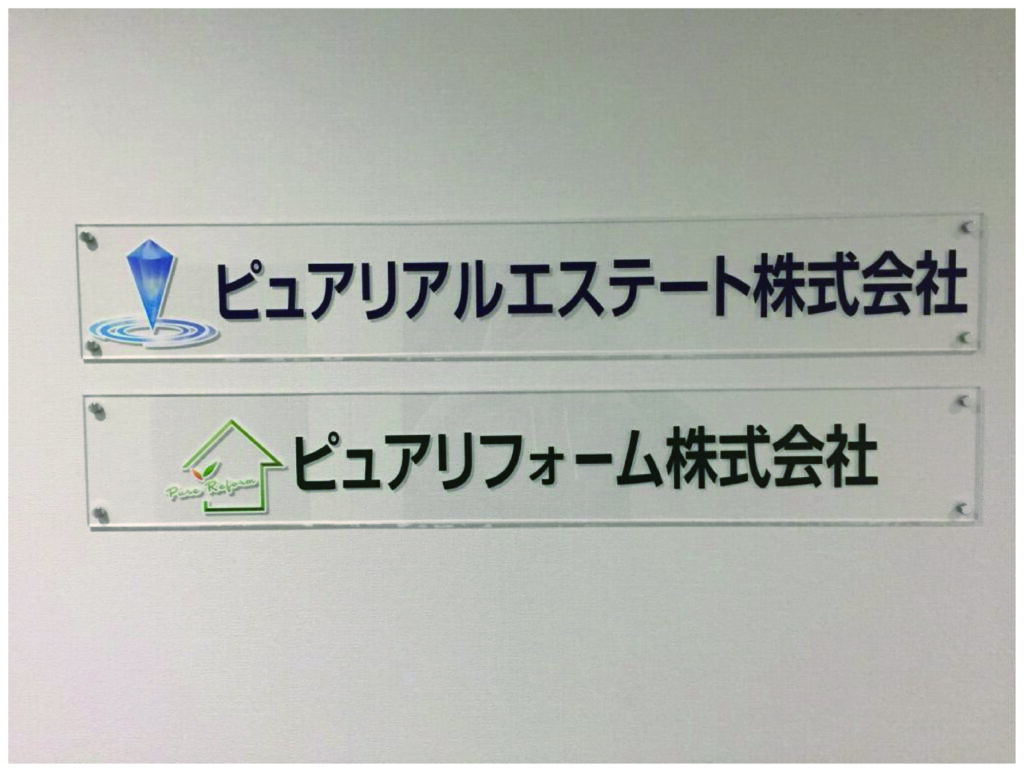 透明アクリル板に切り文字シート（塩ビシート輪郭カット）を貼り付け化粧ビスで壁面固定した屋内エントランスサインの施工事例
